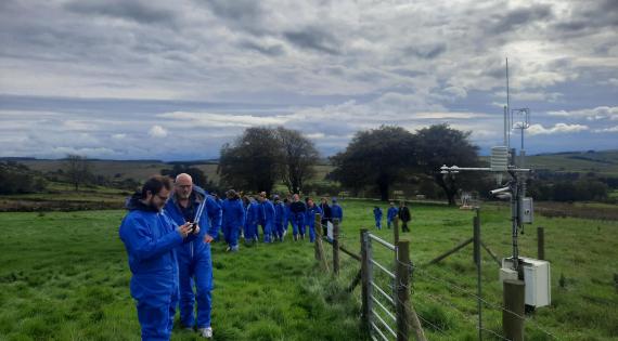 Scientist wearing blue overalls viewing a COSMOS-UK field site